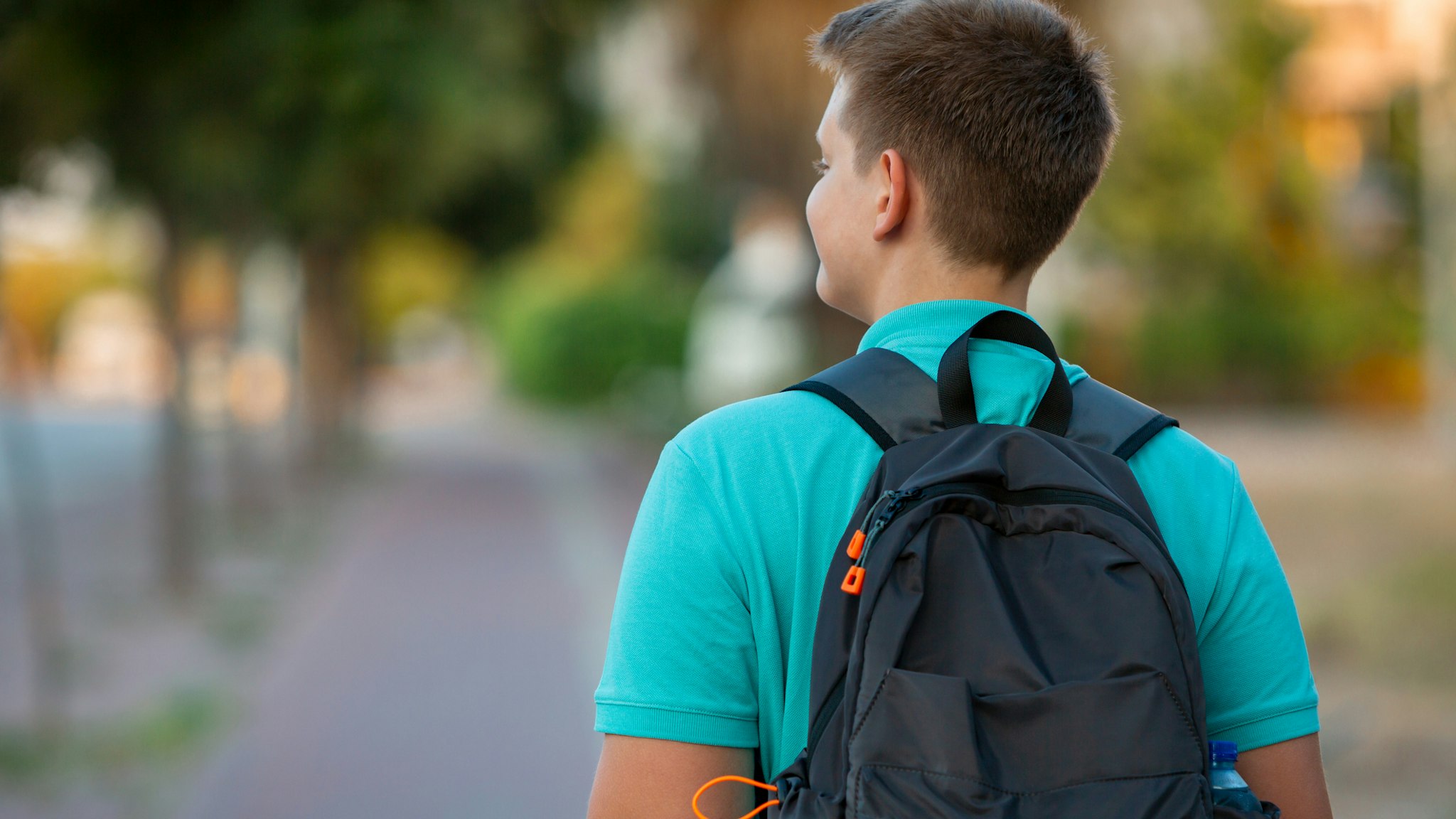 Radiating enthusiasm and dressed in a vibrant turquoise T-shirt, a cheerful teen boy stands ready for school with a backpack in hand. His joyful expression reflects a genuine love for learning as he embraces the excitement of a new day. The warm glow of late daytime enhances the scene, casting a positive light on this junior adventurer's journey into the world of education. This image captures the spirit of youthful exuberance and the anticipation of new discoveries in the school environment.