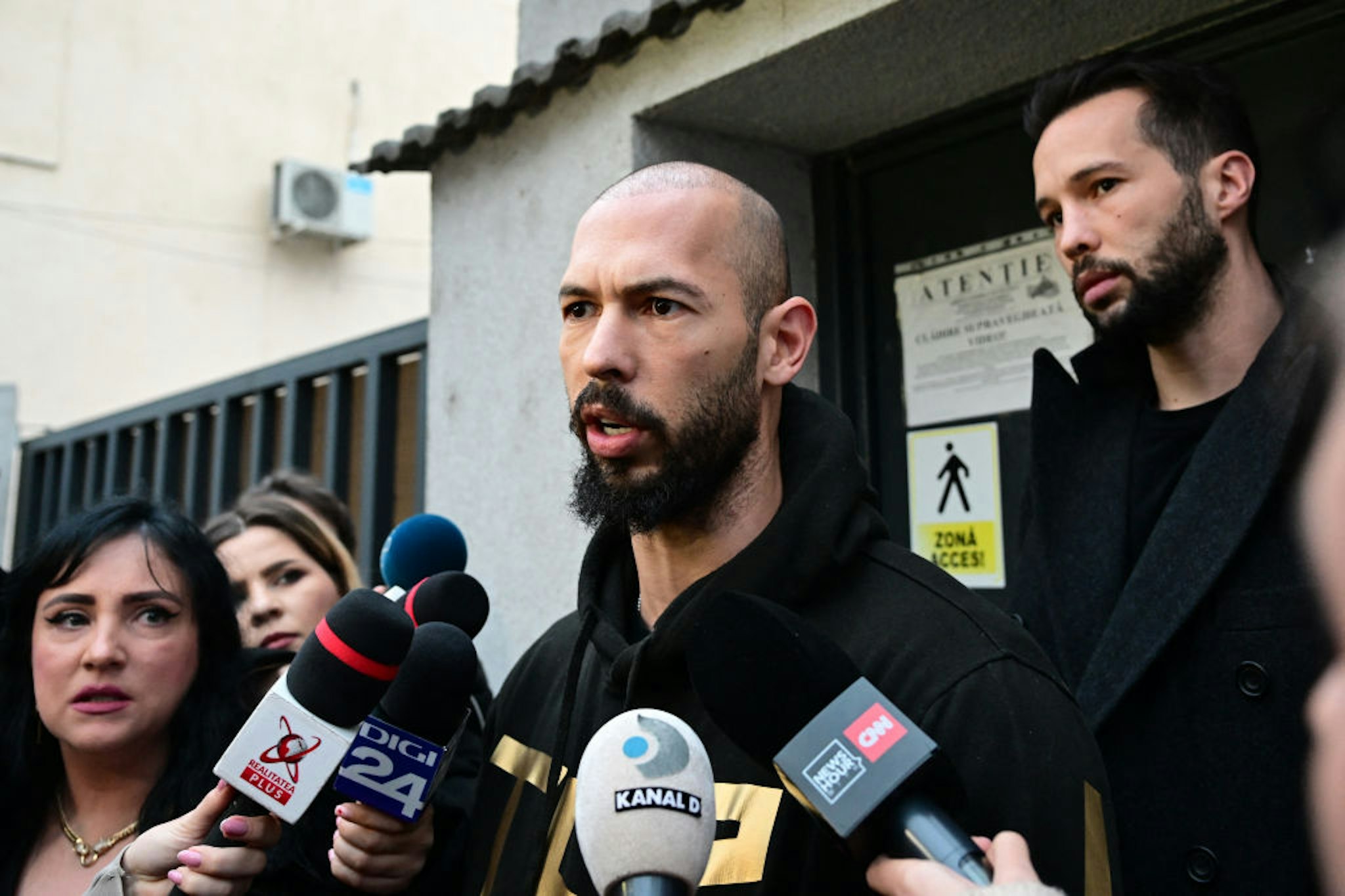 British-US former professional kickboxer and controversial influencer Andrew Tate (C) and his brother Tristan Tate (R) speak to journalists after having been released from detention in Bucharest, Romania on March 12, 2024, after they appeared in a court after Romanian police detained them over UK sex offence charges. A Bucharest court on March 12 granted a request to extradite controversial influencer Andrew Tate to the UK over sex offence charges, but only after the conclusion of legal proceedings in Romania in a separate case. The Bucharest appeals court ruling "orders the execution of the warrant of arrest issued on 19 January 2024" by the Westminster Magistrates' Court, but postpones extradition "until the final resolution of the case" in Romania, which could take years. (Photo by Daniel MIHAILESCU / AFP) (Photo by DANIEL MIHAILESCU/AFP via Getty Images)
