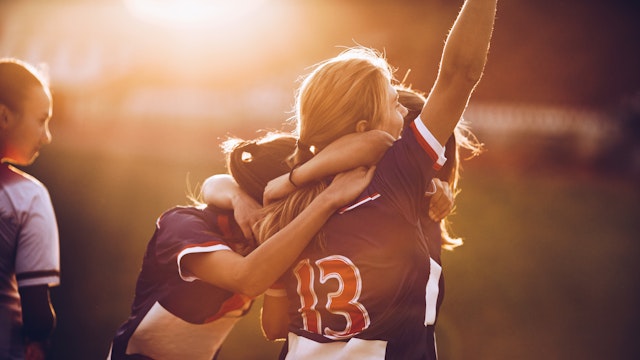 Team of happy female soccer players celebrating their achievement on a playing field at sunset.