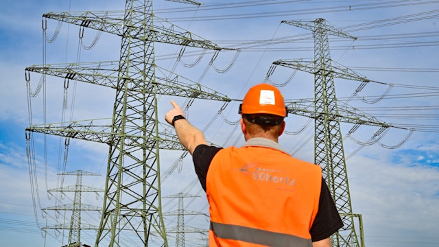 15 March 2024, Brandenburg, Neuenhagen: An employee of grid operator 50Hertz stands on the site of the Neuenhagen substation and points to a high-voltage pylon of the new Nordring Berlin power line. With the Nordring Berlin, 50Hertz is providing another important building block for supplying the greater Berlin and Brandenburg area with renewable energy, thereby strengthening it as an attractive business location. It also strengthens the security of supply in the greater area of the capital and the important grid connection of the steelworks in Hennigsdorf, Brandenburg. A total of 204 pylons were erected and 1800 kilometers of conductor cables stretched along the 75-kilometer route. The investment amounts to around 193 million euros.