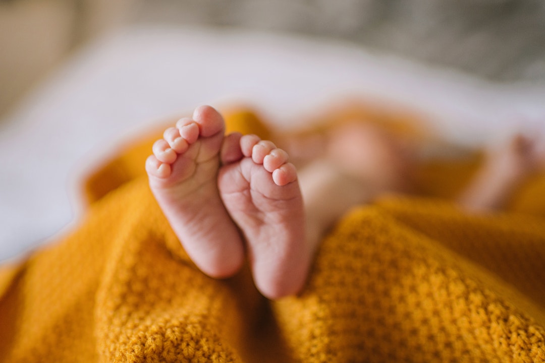 Tiny newborn baby feet in a yellow blanket, infant body, baby care