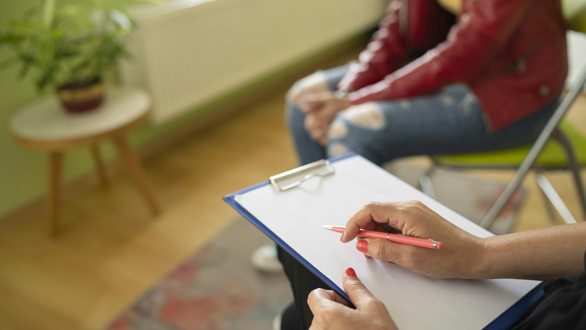 Close up of a female psychologist taking notes and a students knees Close up of a psychologist notes and a students knees during a mental health meeting in a stylish office