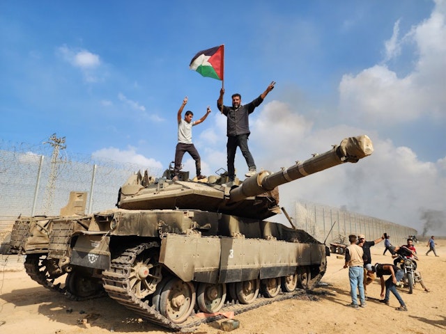 GAZA CITY, GAZA - OCTOBER 07: Hamas' armed wing, the Izz ad-Din al-Qassam Brigades hold a Palestinian flag as they destroy a tank of Israeli forces in Gaza City, Gaza on October 07, 2023. (Photo by Hani Alshaer/Anadolu Agency via Getty Images)