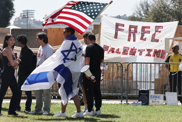 LOS ANGELES, CALIFORNIA - APRIL 30: A counter-demonstrator wears an Israeli flag while carrying an American flag near a pro-Palestinian encampment at the University of California, Los Angeles (UCLA) campus on April 30, 2024 in Los Angeles, California. Pro-Palestinian encampments have sprung up at college campuses around the country with some protestors calling for schools to divest from Israeli interests amid the ongoing war in Gaza. (Photo by Mario Tama/Getty Images)