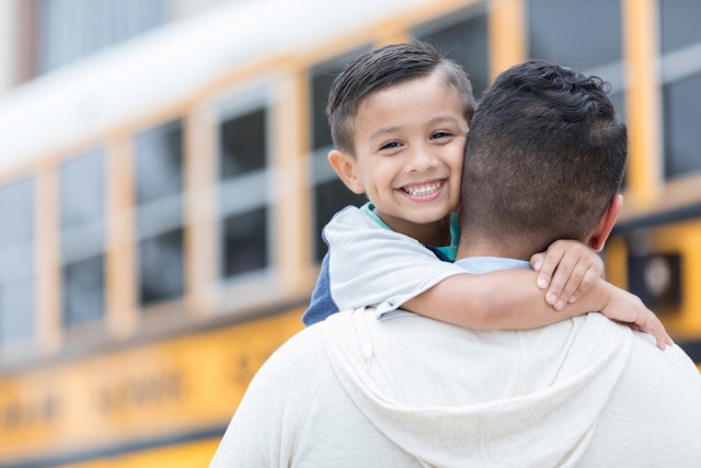 SDI Productions. Getty Images. A confident little boy smiles for the camera as he embraces his father after the first day of school. He has just ridden the school bus home.
