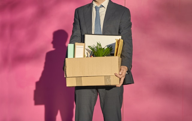 Westend61. Getty Images. Businessman carrying box with personal belonging on sunny day.
