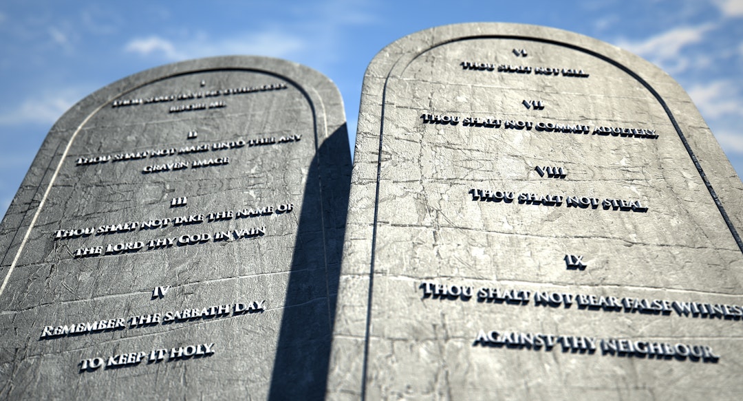 Two stone tablets with the ten commandments inscribed on them standing in brown desert sand infront of a blue sky. allanswart. Getty Images.