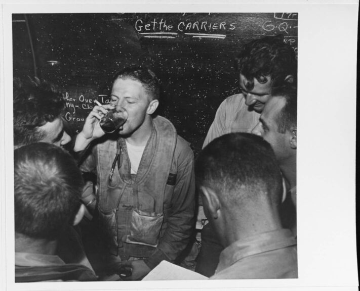 Battle of the Philippine Sea, June 1944. Lieutenant Ronald P. Rip Gift relaxes with other pilots in a ready room on board USS Monterey (CVL-26), after landing on her at night following strikes on the Japanese fleet, 20 June 1944. Note admonition Get the Carriers on chalk board in the background. Photographed by Lieutenant Victor Jorgensen, USNR. Official U.S. Navy Photograph, now in the collections of the National Archives. Catalog #: 80-G-474791