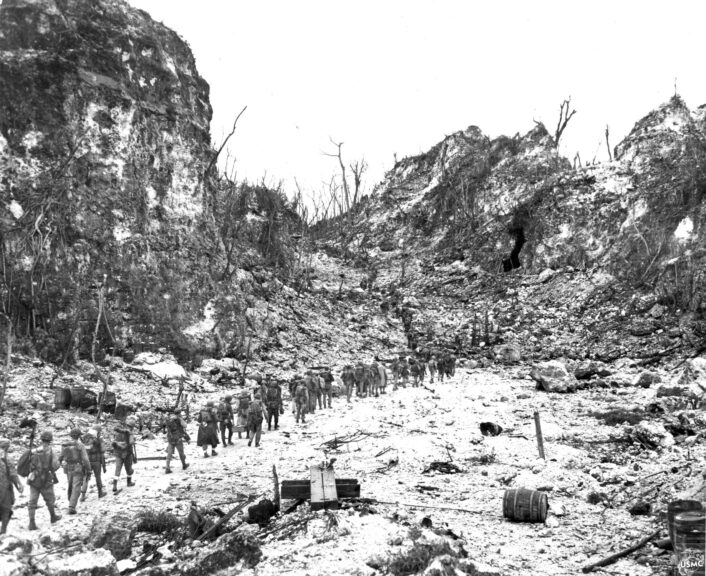 A column of Marines marches toward the front line through a defile at the southwestern end of Peleliu's Bloody Nose Ridge. (U.S. Marine Corps). U.S. Naval Institute.