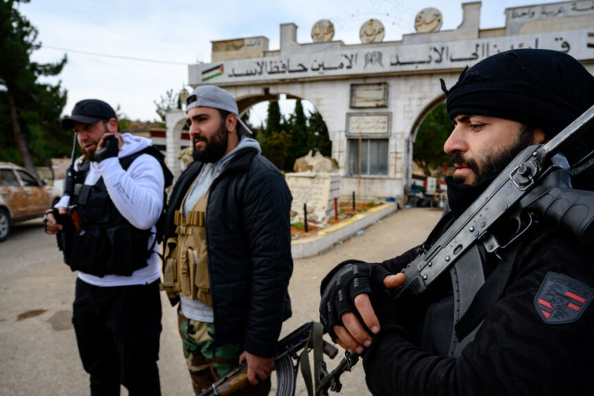 UNSPECIFIED, SYRIA - DECEMBER 11: Islamist rebels of the Hayat Tahrir al-Sham (HTS) stand guard at the entrance of the first abandoned military base that reads Our Leader Forever - Hafez al-Assad on December 11, 2024, inside Lebanons border with Syria, Rebel forces in Syria have retaken the capital from longtime ruler Bashar al-Assad, who has fled the country for Moscow. The fall of the Assad regime marks a new chapter for Syria, which has been mired in a multi-party civil war since 2011, sparked by the Arab Spring uprisings. (Photo by Scott Peterson/Getty Images)