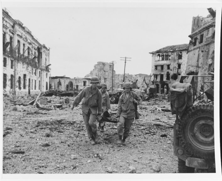 Liberation of Manila, 1945. Stretcher party brings out a wounded U.S. soldier, following an attack by U.S. troops to liberate Filipino prisoners in the walled city, 23 February 1945. Note wrecked buildings. Catalog #: 80-G-273406. National Archives. Naval History and Heritage Command.