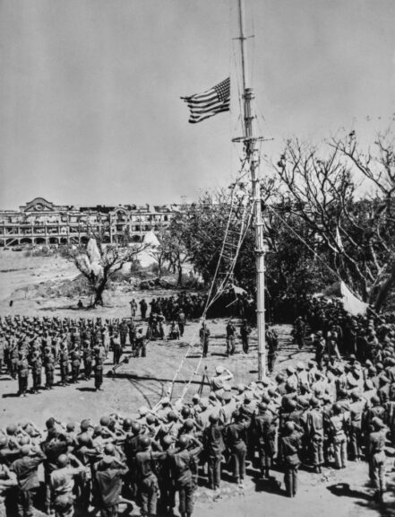 Parachutes discarded by airborne troops still hang from the tree tops as the US flag is raised over Corregidor following the island's recapture, Philippines, March 2nd 1945. General MacArthur stands to the left of the flagpole, saluting as the colours are hoisted. (Photo by Central Press/Hulton Archive/Getty Images)