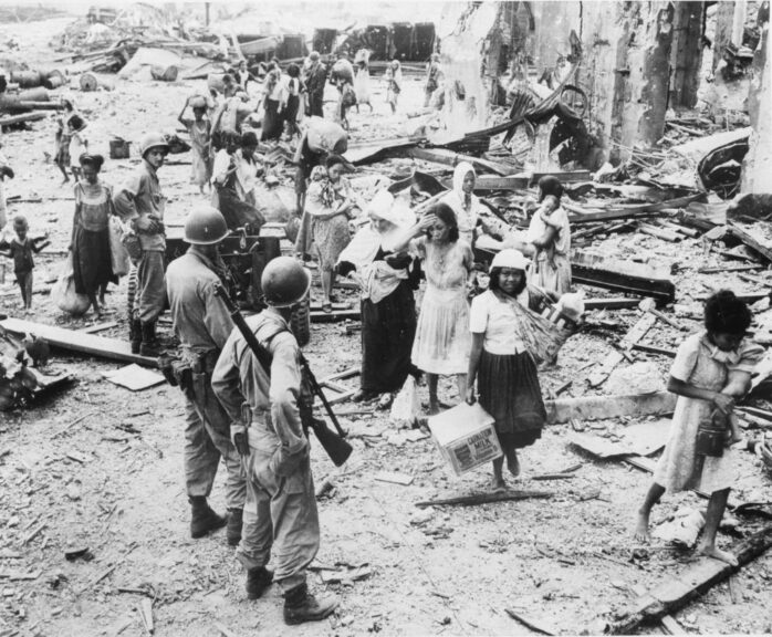 20th March 1945: American soldiers watching as refugees pick their way through the debris of North Manila, after safely arriving in the American held part of the city while fighting continues elsewhere. (Photo by Central Press/Getty Images)