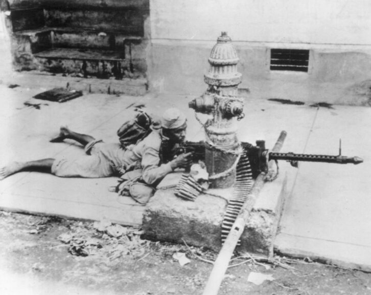 February 1945: A Filipino guerrilla fighting Japanese forces of occupation in Manila. Lacking a tripod for his machine-gun, he has tied the weapon to a fire hydrant. (Photo by Keystone/Getty Images)