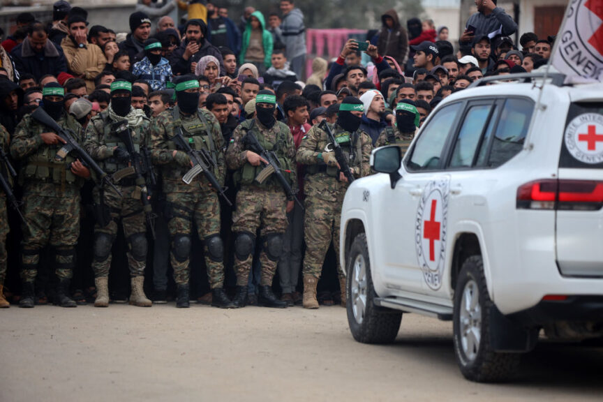 Hamas fighters stand in formation as Palestinians gather on a street to watch the handover of three Israeli hostages to a Red Cross team in Deir el-Balah, central Gaza, on February 8, 2025. Hamas militants hand over three Israeli hostages on February 8, as part of the fifth exchange under a fragile Gaza ceasefire, with 183 prisoners held by Israel due to be released later in the day. (Photo by Majdi Fathi/NurPhoto via Getty Images)