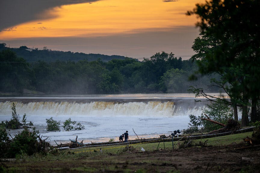 CENTER POINT, TEXAS - JULY 06: People stand together beyond caution tape on the banks of the Guadalupe River on July 06, 2025 in Center Point, Texas. Heavy rainfall caused severe flooding along the Guadalupe River in central Texas, leaving more than 70 people reported dead. (Photo by Brandon Bell/Getty Images)