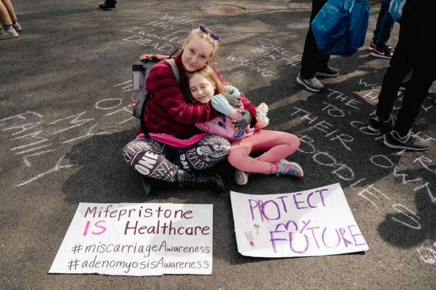 Abortion advocate Laura Klime Coates of Baltimore embraces her daughter, Charlize, 9, as they pose for a portrait with her sign outside the Supreme Court in Washington, DC, on March 26, 2024. (Photo by Shuran Huang for The Washington Post via Getty Images)