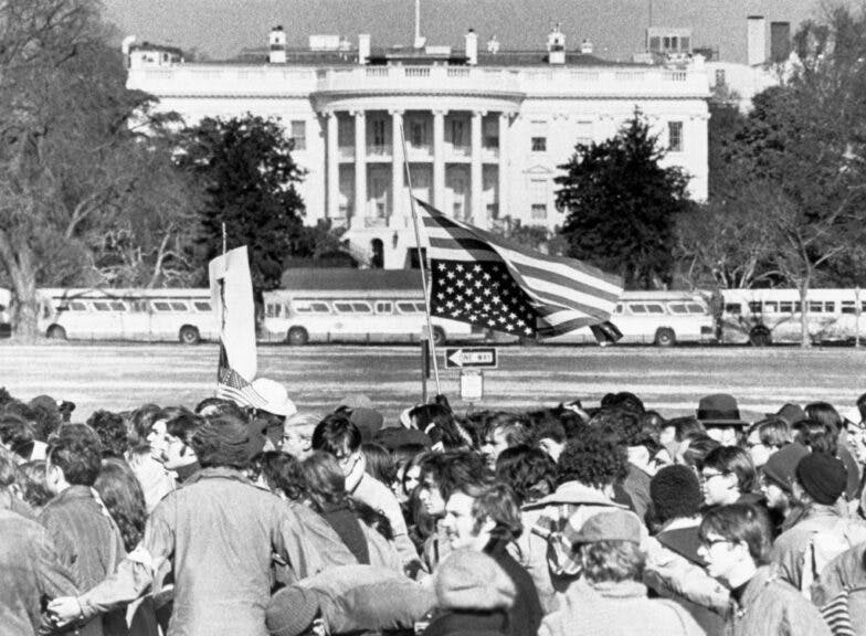 A demonstrator carries an American flag upside down as the peace march passes its nearest point to the White House. Buses parked bumper to bumper in the background were used as barricades. No one was allowed closer than one block from the Executive Mansion where President Nixon was conducting business as usual.(Photo by Bettmann Archive/Getty Images)