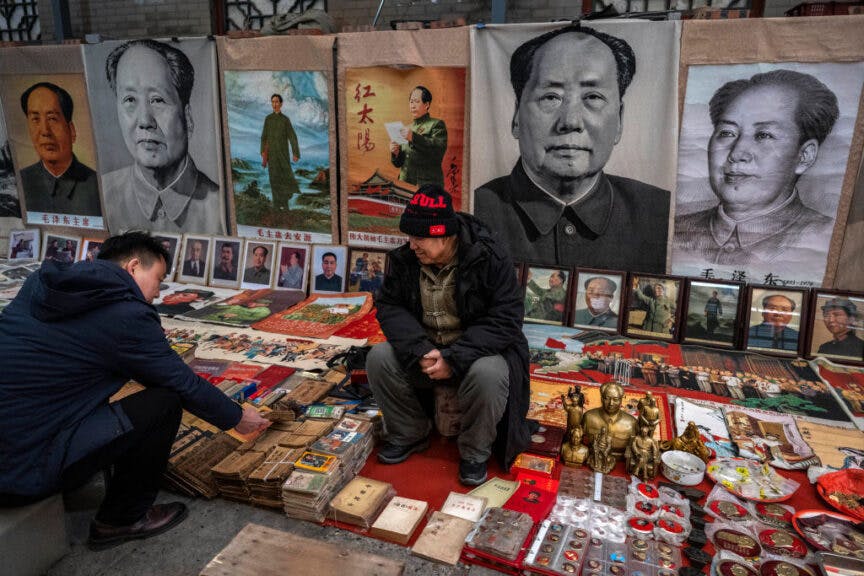 BEIJING, CHINA - DECEMBER 06: Large images of the late former leader Mao Zedong hang behind a vendor as a customer looks at items at a stall at the Panjiayuan Market on December 6, 2024 in Beijing, China. (Photo by Kevin Frayer/Getty Images)